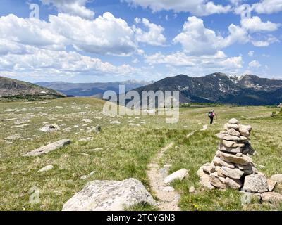 Einsame Wanderer auf einem Pfad mit Steinmarkierungen inmitten der riesigen alpinen Weite des Rocky Mountain National Park. Stockfoto