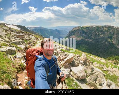 Ein Wanderer fängt einen fröhlichen Moment auf dem North Inlet Trail ein, mit der atemberaubenden Kulisse der alpinen Ausblicke des Rocky Mountain National Park. Stockfoto