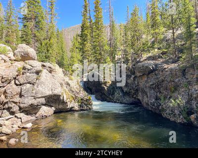 Der ruhige Big Pool, eingebettet zwischen zerklüfteten Klippen und umgeben von Kiefern, spiegelt die ruhige Schönheit des Rocky Mountain National Park wider. Stockfoto