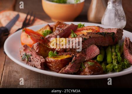 Geschnittenes Rumpsteak mit cajun-Kartoffeln, Spargel und Kräutern und einer Knoblauchbutter-Sauce. Stockfoto