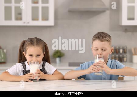 Niedliche Kinder trinken frische Milch aus Gläsern am weißen Tisch in der Küche Stockfoto