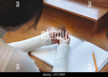 Eine Frau, die an Alopezie leidet, hält ihr Haar in den Händen Stockfoto