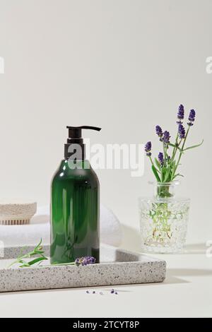 Nahaufnahme einer labelllosen, transparenten, grünen Shampoo-Flasche, die auf einem grauen Tablett neben einer Vase mit Lavendelblüten steht und sich gegen ein W abhebt Stockfoto