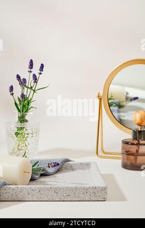 Lavendelblüten in einer Glasvase auf einem grauen Tablett mit Kerzen und Handtüchern, und ein Diffusor ätherischer Öle wird neben einem Spiegel auf einer weißen Ba platziert Stockfoto