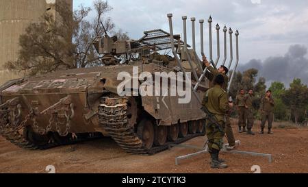 Israelische Soldaten errichteten eine Hanukka-Menora, um die sechste Kerze des sechsten Tages des jüdischen Hanukka-Feiertags an einer Stelle nahe der Grenze zu Gaza anzuzünden, während die Kämpfe zwischen Israel und der militanten Gruppe Hamas am 12. Dezember 2023 an der Grenze zu Gaza, Israel. Seit den Angriffen der Hamas vom 7. Oktober sind mehr als zwei Monate vergangen, die Israels Luft- und Bodenkampagne im Gazastreifen ausgelöst haben. Stockfoto