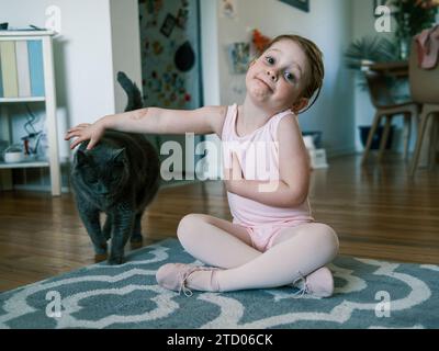 Glückliches Kleinkind im Ballettoutfit, das eine Katze streichelt Stockfoto