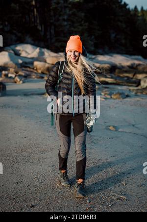 Smiling woman in orange hat hikes along beach on Maine coast Stock Photo