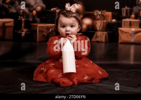 Ein Mädchen mit großen Augen, das an weihnachten auf einer Milchflasche kaut Stockfoto