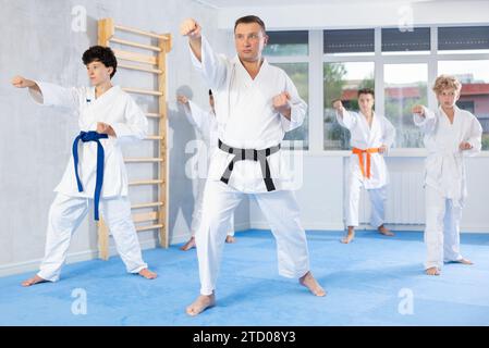 Trainer mittleren Alters, der Kata in Reihe mit Jugendlichen Teilnehmern von Karatekursen übt Stockfoto