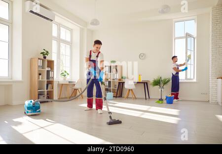 Gruppe junger glücklicher männlicher Menschen in Uniform, die das Kundenhaus abwischen, waschen und saugen. Stockfoto