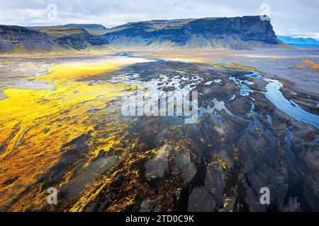 Ein Luftbild fängt das atemberaubende Flussbecken in Island vor der dramatischen Kulisse aus zerklüfteten Klippen und pulsierendem, goldenem Gelände ein Stockfoto