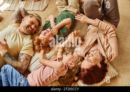 Blick von oben auf die überfröhlichen Eltern und Kinder, die sich auf dem Boden im modernen Wohnzimmer amüsieren, schöne Momente Stockfoto