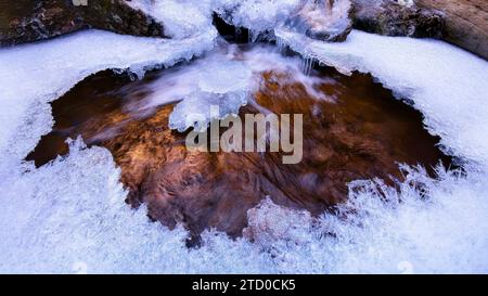 Ein Winter-Whirlpool, der in Eis mit bunten Steinen bedeckt ist, die durch die klare, vereiste Oberfläche sichtbar sind Stockfoto