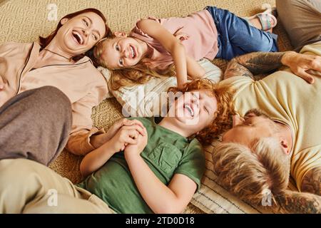 Blick von oben auf lachende Eltern und Kinder, die sich auf dem Boden und im modernen Wohnzimmer amüsieren Stockfoto