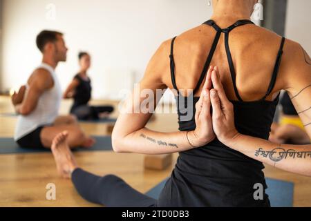 Eine Nahaufnahme des Rückens einer Frau, während sie Yoga in einer Klasse übt, Hände in Namaste Position. Stockfoto