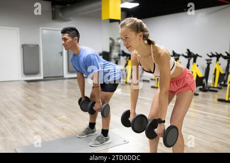 Ein junges Paar trainiert gemeinsam und hebt Gewichte in einem gut ausgestatteten Fitnessstudio mit Fokus und Entschlossenheit. Stockfoto