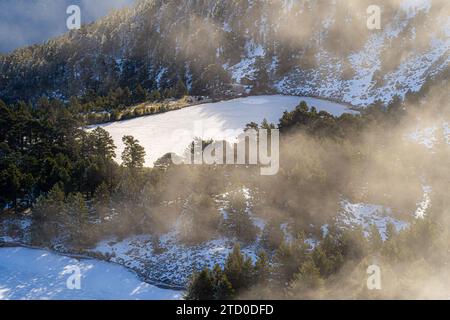 Aus der Vogelperspektive auf schneebedeckten Hang mit Nadelbäumen unter Wolken im Sonnenlicht in der Gletscherlagune von Neila Spanien Europa Stockfoto