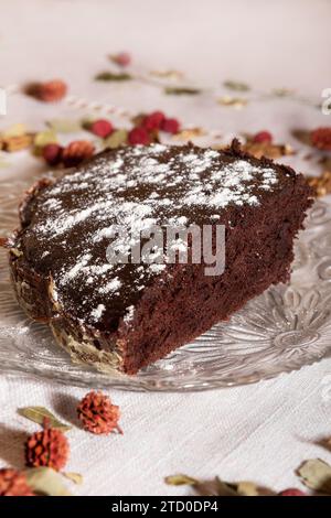 Hoher Winkel verführerischer Schokoladenkuchen, mit Puderzucker bestreut, elegant auf einem Glasteller mit einem dekorierten Tischhintergras präsentiert Stockfoto