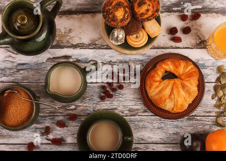 Blick von oben auf einen Holztisch mit Tassen Tee, einer Teekanne, Kuchen und verstreuten getrockneten Blättern, die eine gemütliche herbstliche Atmosphäre hervorrufen. Stockfoto