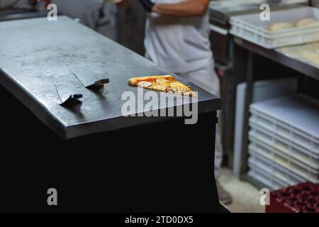 Ein Stück frisch zubereitete Pizza mit Stahlspateln auf einer Metalltheke in der Küche des Restaurants Stockfoto