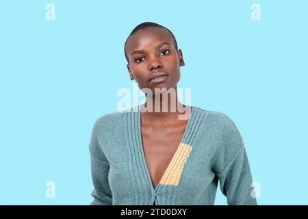 Porträt einer jungen afroamerikanischen Frau in blauem Pullover mit kurzen schwarzen Haaren, die in die Kamera auf blauem Hintergrund schauen Stockfoto