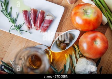 Hochwertiges Bild mit verschiedenen frischen Zutaten, darunter geschnittene Tomaten, iberischer Schinken, Olivenöl, Oliven, Spargel, Knoblauch und Rosmarin spr Stockfoto