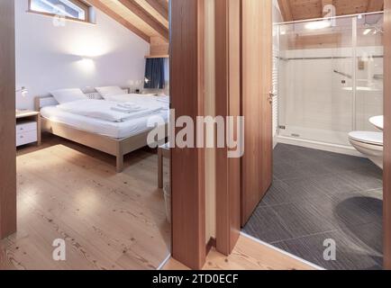 Ein gepflegtes Schlafzimmer und Bad mit einem großen Bett mit weißer Bettwäsche und einem eigenen Bad, das in einem sauberen, modernen Design mit Wo-Effekt gehalten wird Stockfoto