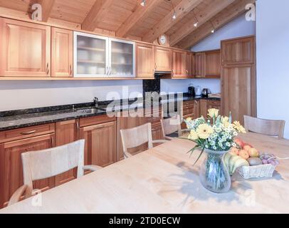 Die Küche der Alpenkabine verfügt über Holzschränke, Granitarbeitsflächen und einen Tisch mit frischem Obst und Blumen. Stockfoto