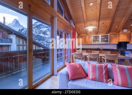 Ein warmes und einladendes Chalet-Wohnzimmer mit großen Fenstern, die das berühmte Matterhorn in Zermatt, Schweiz, umrahmen. Stockfoto