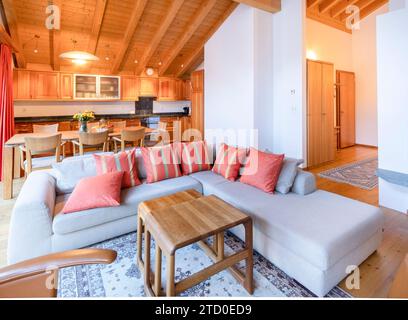 Ein einladendes Wohnzimmer in einem Chalet mit einem weichen Sofa, Holzmöbeln und einer Kochnische in gemütlicher, moderner alpiner Einrichtung. Stockfoto