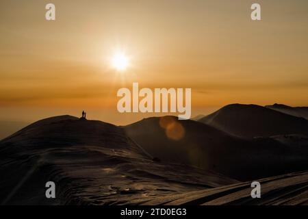 Ganzkörper der Silhouette nicht erkennbare Person mit Snowboard, die auf dem Berg vor dem Himmel steht und während des Sonnenuntergangs in Japan im Winter helle Sonne hat Stockfoto