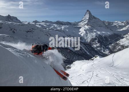 Seitenansicht eines anonymen Skiläufers in Schutzkleidung, der von schneebedecktem Bergvorsprung unter blauem Himmel in Zermatt, Schweiz, springt Stockfoto