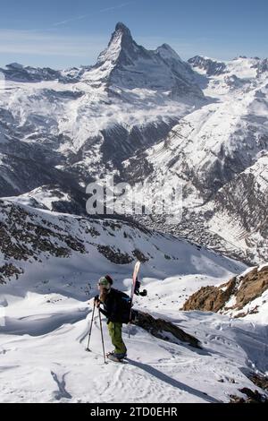 Hoher Winkel der Reisenden in warmer Kleidung mit Snowboard mit Trekkingstöcken, während Sie die schneebedeckten Berge in Zermatt, Schweiz unter bewundern Stockfoto