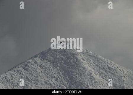 Aus der Ferne sehen Sie eine nicht erkennbare Gruppe von Menschen, die auf einem schneebedeckten Berg vor bewölktem Himmel stehen, während Sie den Urlaub in Japan genießen Stockfoto
