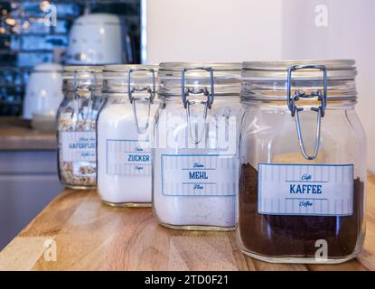 Vier Gläser mit Metallverschlüssen auf einer Holztheke, die mit Zutaten in deutscher Sprache beschriftet sind. Stockfoto