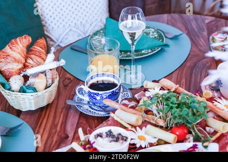 Ein gut ausgestatteter Brunch-Tisch mit einer Vielzahl von Speisen, darunter frische Croissants, Aufschnitt und Käse, begleitet von Kaffee, Saft, und Wein. Stockfoto