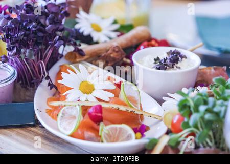 Ein farbenfroher Gourmet-Brunch mit Räucherlachs, essbaren Blumen, frischem Gemüse, Dip und Zitrusscheiben. Stockfoto