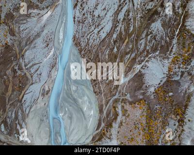 Aus der Vogelperspektive auf einen sich schlängelnden Gletscherfluss, der durch eine zerklüftete Landschaft fließt. Stockfoto