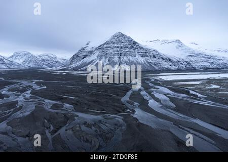 Majestätische schneebedeckte Berge erheben sich im Winter über einen sich windenden Fluss in der einsamen Landschaft Islands. Stockfoto