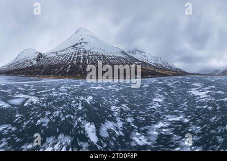 Panoramablick auf einen gefrorenen See mit schneebedeckten Bergen im Hintergrund unter einem bewölkten Himmel in Island. Stockfoto