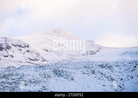 Ein ruhiger Blick auf einen schneebedeckten Berg vor einem weichen, pastellfarbenen Himmel in der eisigen Wildnis Islands. Stockfoto