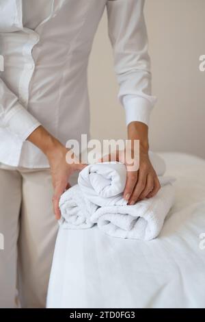 Schnitthand einer anonymen Massagetherapeutin in weißer Uniform stehend und mit sauberen aufgerollten Handtüchern während der Arbeit im Spa-Salon Stockfoto