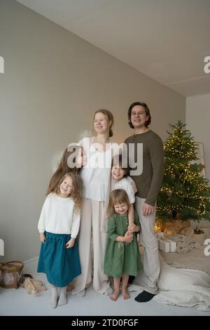 Eine glückliche Familie posiert für ein Weihnachtsfoto vor einem Weihnachtsbaum und zeigt eine warme, festliche Atmosphäre. Stockfoto