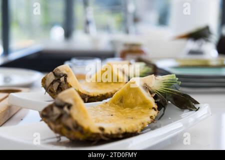 Appetitlich frische Ananasscheiben mit Dornschale und grünen Blättern, während sie auf weißen Teller auf Küchentisch mit Ovar und Kern entfernt Agi gelegt werden Stockfoto