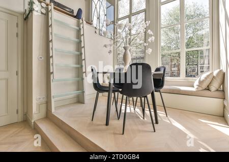 Weiße Blumen in Vase auf Esstisch, umgeben von Stühlen in der Nähe der Leiter und Platz am Fenster im Apartment Stockfoto