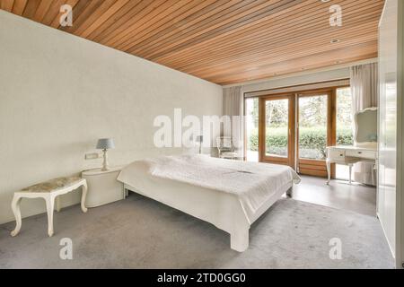 Komfortables Bett mit warmer Decke neben Fenster und Tür zum Hinterhof in stilvollem Schlafzimmer mit grauen Wänden Stockfoto