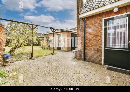 Bäume und Pflanzen im Garten im Hinterhof mit leerer gepflasterter Terrasse vor dem modernen Haus mit Tür und Ziegelmauer Stockfoto