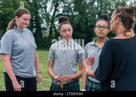 Eine Gruppe Mädchen in einer britischen High School steht draußen und spricht mit einem Lehrer und Mentor. Stockfoto