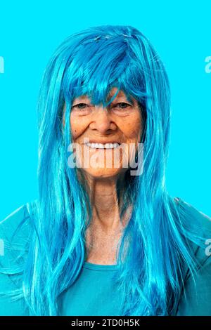 Porträt einer positiven älteren Frau mit blauer Perücke und T-Shirt, die im Studio vor blauem Hintergrund in die Kamera blickt Stockfoto