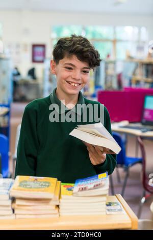 Ein männlicher Schüler checkt ein Buch in der Schulbibliothek mit dem Bibliothekar Stockfoto